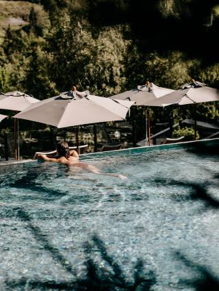 Entspannung und Erholung - Person genießt den Ausblick vom Hotelpool in die Natur