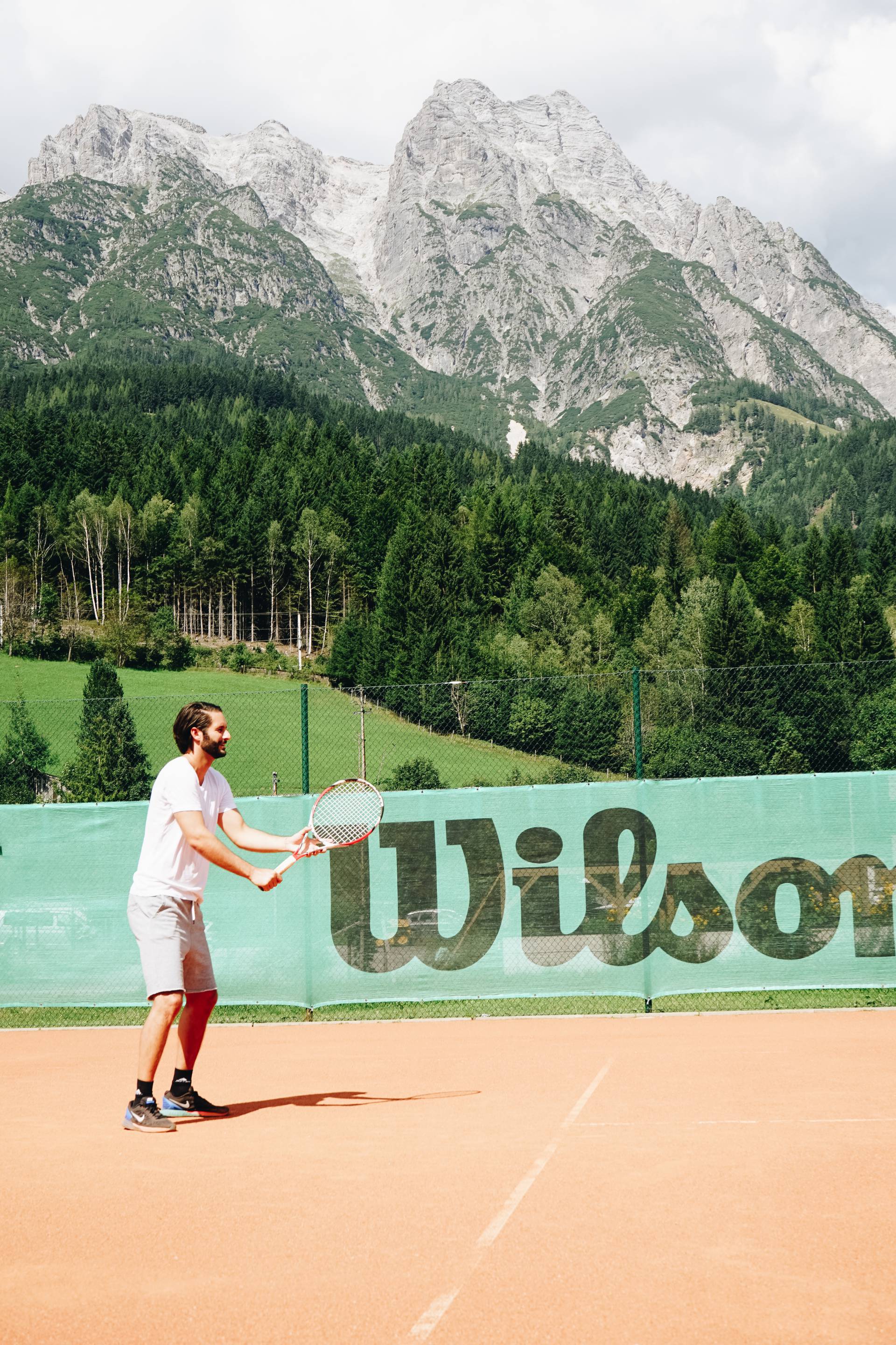 Mann spielt Tennis vor den Leoganger Steinbergen im Naturhotel Forsthofgut