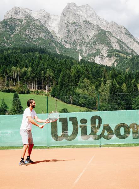 Mann spielt Tennis vor den Leoganger Steinbergen im Naturhotel Forsthofgut