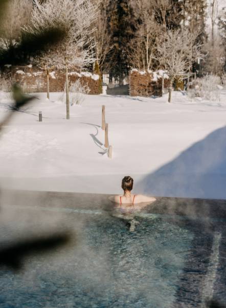 Woman in outdoor pool looking at snowy landscape